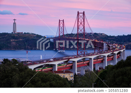View of Lisbon view from Miradouro do Bairro do Alvito viewpoint of Tagus river, traffic with light trails on 25th of April Bridge, and Christ the King statue in the evening twilight. Lisbon, Portugal 105851280
