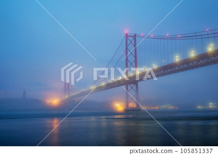 View of 25 de Abril Bridge famous tourist landmark of Lisbon connecting Lisboa and Almada in heavy fog mist wtih yacht boats passing under. Lisbon, Portugal View of 25 de Abril Bridge famous tourist landmark of Lisbon connecting Lisboa and Almada in heavy fog mist wtih yacht boats passing under. Lisbon, Portugal 105851337