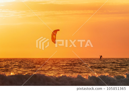 Foiling kiteboarding kitesurfing kiteboarder (kitesurfer) silhouette in the Atlantic ocean on sunset. Fonte da Telha beach, Costa da Caparica, Portugal Foiling kiteboarding kitesurfing kiteboarder (kitesurfer) silhouette in the Atlantic ocean on sunset. Fonte da Telha beach, Costa da Caparica, Portugal 105851365