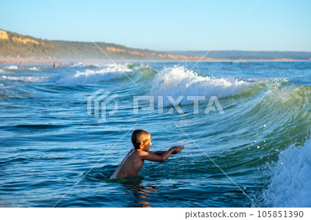 Boy has fun enjoys jumps dives in ocean sea waves of Atlantic Ocean. Fonta da Telha beach, Costa da Caparica, Portugal 105851390