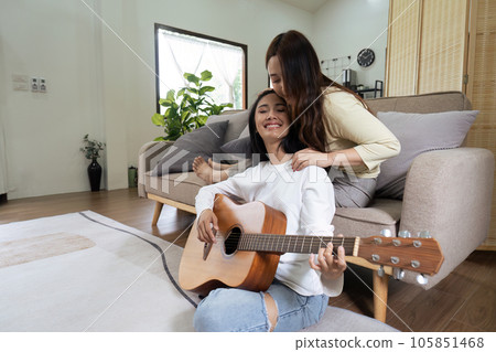 LGBT lesbian gay couple playing guitar and singing with romantic feelings at home LGBT lesbian gay couple playing guitar and singing with romantic feelings at home 105851468