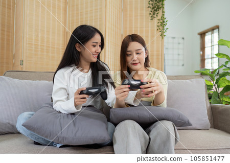 Asian beautiful lesbian gay couple enjoy play game together in Livingroom. Two female friend sit on sofa in living room, feel happy to play joystick game at home. 105851477