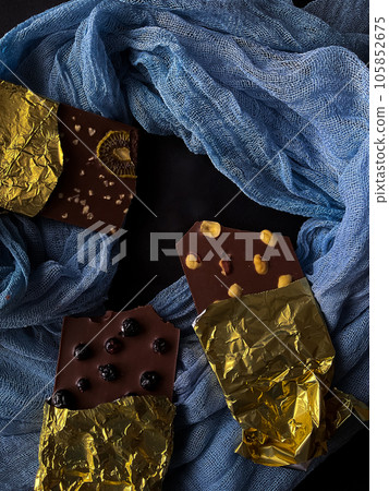 Chocolate with berries, kiwi, nuts in gold foil on blue and black background Chocolate with berries, kiwi, nuts in gold foil on blue and black background 105852675