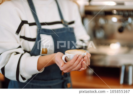 Barista holds cup with coffee in his hands. Drawing is drawn on coffee foam. Food and drink concept. Barista holds cup with coffee in his hands. Drawing is drawn on coffee foam. Food and drink concept. 105855167