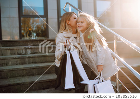 Young mother and little girl with shopping bags after shopping. Spring Style. Consumerism. Young mother and little girl with shopping bags after shopping. Spring Style. Consumerism. 105855516