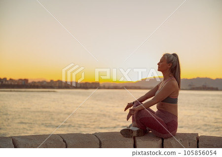 Asian sportswoman practicing yoga, sitting on edge at seashore 105856054