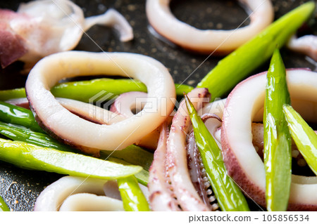 A close-up of a cooking scene in which squid (boiled squid) and garlic sprouts are fried in a frying pan. 105856534