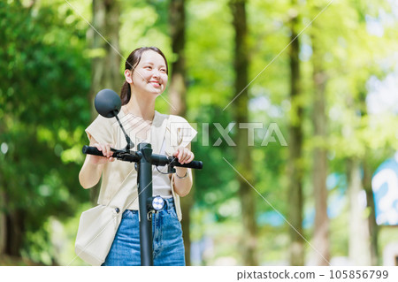 A young woman running on a tree-lined street with an electric kickboard 105856799