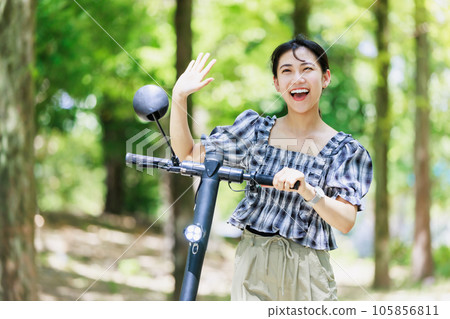 一位年輕女子在綠樹成蔭的街道上騎著電動浮板 105856811
