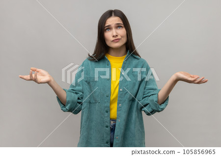 I don't know. Portrait of confused beautiful young woman standing, raised arms, confused and thinking, wearing casual style jacket. Indoor studio shot isolated on gray background. I don't know. Portrait of confused beautiful young woman standing, raised arms, confused and thinking, wearing casual style jacket. Indoor studio shot isolated on gray background. 105856965