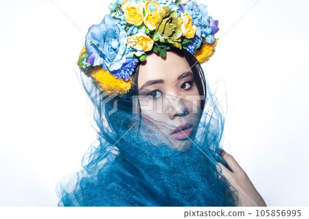 Closeup portrait of sensual beautiful young adult woman with floral hat and blue veil, looking at camera with serious expression. Indoor studio shot isolated on gray background, 105856995