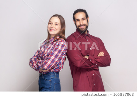Portrait of smiling cheerful woman and man standing together with crossed hands, looking at camera with toothy smile, being in good mood. Indoor studio shot isolated on gray background. Portrait of smiling cheerful woman and man standing together with crossed hands, looking at camera with toothy smile, being in good mood. Indoor studio shot isolated on gray background. 105857068