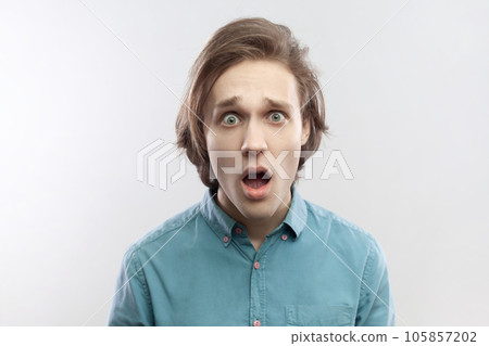 Portrait of shocked amazed astonished young man looking at camera with big eyes and open mouth, sees something amazing, wearing blue shirt. Indoor studio shot isolated on gray background. Portrait of shocked amazed astonished young man looking at camera with big eyes and open mouth, sees something amazing, wearing blue shirt. Indoor studio shot isolated on gray background. 105857202