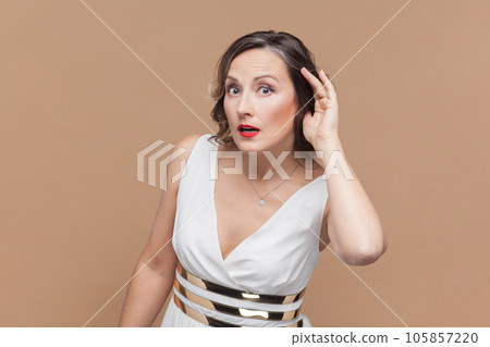 Can't hear you. Attentive middle aged woman holding hand near ear trying to listen quiet conversation, overhearing gossip, having hearing problems Indoor studio shot isolated on light brown background Can't hear you. Attentive middle aged woman holding hand near ear trying to listen quiet conversation, overhearing gossip, having hearing problems Indoor studio shot isolated on light brown background 105857220