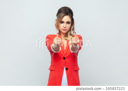 Portrait of serious strict beautiful blonde woman standing showing rude impolite gesture, middle finger gesture, wearing red jacket. Indoor studio shot isolated on gray background. 105857221