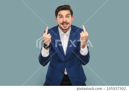 Rude impolite handsome man with mustache standing showing middle fingers, looking at camera with clenched teeth, wearing white shirt and jacket. Indoor studio shot isolated on light blue background. 105857302