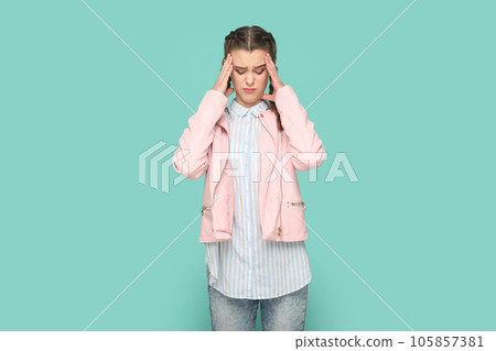 Portrait of sick ill unhealthy teenager girl with braids wearing pink jacket standing massaging her temples, having headache and flu symptoms. Indoor studio shot isolated on green background. 105857381