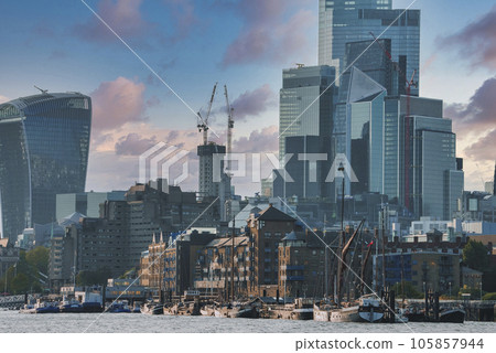 Sailing barge moored at harbor of Thames river. Modern skyscrapers with cloudy sky in background. Scenic view of capital city of London during sunny day. 105857944