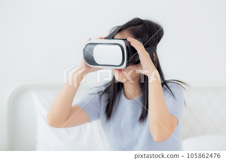 Young asian woman wearing vr headset playing game with excited on bed in the bedroom. Young asian woman wearing vr headset playing game with excited on bed in the bedroom. 105862476