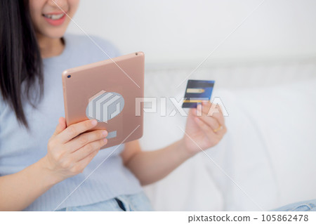 Closeup hands young woman sitting on bed using digital tablet shopping online with credit card. Closeup hands young woman sitting on bed using digital tablet shopping online with credit card. 105862478
