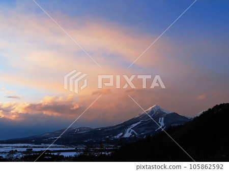 At dusk in winter, Mt. Bandai shines with clouds dyed red by the setting sun and a snow cap. The contest is impressive and beautiful against the blue sky. 105862592
