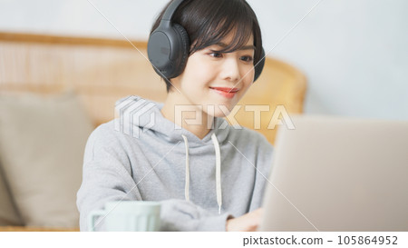 一位女士在電腦上工作，同時戴著耳機聽音樂 105864952