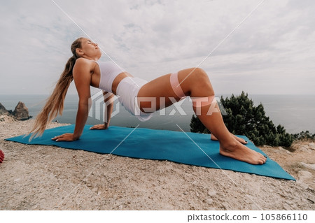 Woman sea pilates. Sporty, middle-aged woman practicing pilates in park near the sea. trains on a yoga mat and exudes a happy and active demeanor. healthy lifestyle through exercise and meditation. Woman sea pilates. Sporty, middle-aged woman practicing pilates in park near the sea. trains on a yoga mat and exudes a happy and active demeanor. healthy lifestyle through exercise and meditation. 105866110