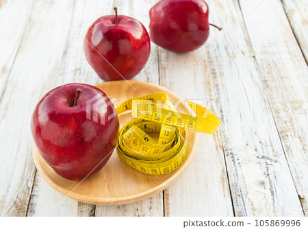 Red apple and yellow tape measure on a wooden table Red apple and yellow tape measure on a wooden table 105869996