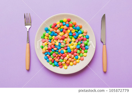 cutlery on table and sweet plate of candy. Health and obesity concept, top view on colored background cutlery on table and sweet plate of candy. Health and obesity concept, top view on colored background 105872779