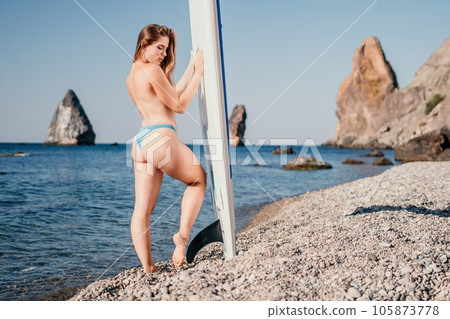 Woman sea sup. Close up portrait of beautiful young caucasian woman with long hair looking at camera and smiling. Cute woman portrait in a white bikini posing on sup board in the sea Woman sea sup. Close up portrait of beautiful young caucasian woman with long hair looking at camera and smiling. Cute woman portrait in a white bikini posing on sup board in the sea 105873778