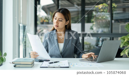 Asian businesswomen sit at their desks and calculate financial graphs showing results about their investments, planning successful business growth process Asian businesswomen sit at their desks and calculate financial graphs showing results about their investments, planning successful business growth process 105874068
