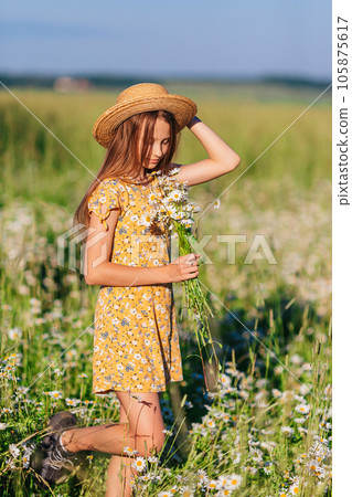 Portrait of girl in a yellow dress and straw hat on a chamomile field in summer 105875617