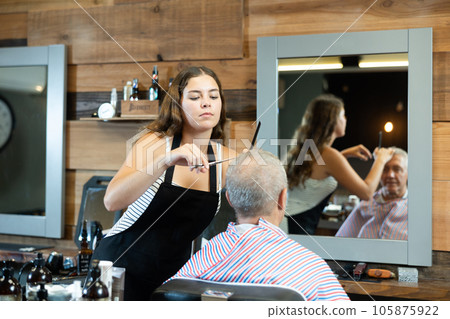 Hairdresser cutting hair of male client. Hairstylist serving client at barber shop 105875922
