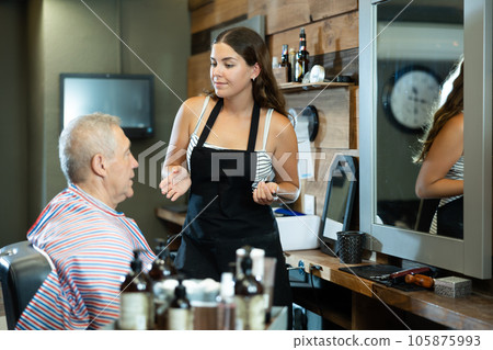Young female barber discussing haircut with elderly client in barbershop Young female barber discussing haircut with elderly client in barbershop 105875993