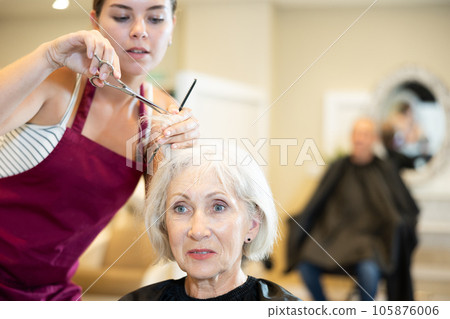 Young woman master completes creation of senior female clients image with help of scissors Young woman master completes creation of senior female clients image with help of scissors 105876006