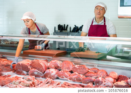 Elderly butcher shop owner standing behind display case with meat Elderly butcher shop owner standing behind display case with meat 105876016