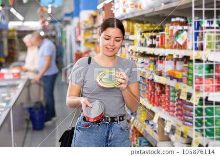 Young female shopper choosing canned food in supermarket 105876114