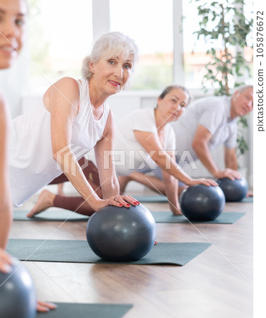 Group of mature active people doing soft ball exercises during group pilates class in fitness studio 105876672