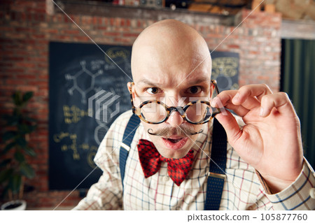 Close-up of balm man in glasses with moustaches looking at camera with attention. Scientist in classroom Close-up of balm man in glasses with moustaches looking at camera with attention. Scientist in classroom 105877760