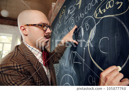Young man, scientist standing by blackboard with formulas and calculations. Chemistry lessons 105877768