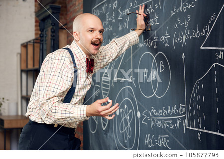 Excited man, professor, scientist standing by blackboard with scientific formulas and calculations. Math, physics, chemistry lessons Excited man, professor, scientist standing by blackboard with scientific formulas and calculations. Math, physics, chemistry lessons 105877793