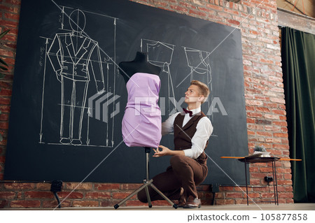 Talented man, fashion designer working in ateliers, creating beautiful dress, making measurements on mannequin Talented man, fashion designer working in ateliers, creating beautiful dress, making measurements on mannequin 105877858