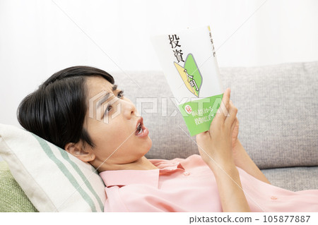 Woman reading investment book on sofa 105877887