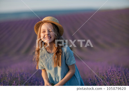 Lavender sunset girl. A laughing girl in a blue dress with flowing hair in a hat walks through a lilac field, holds a bouquet of lavender in her hands. 105879620
