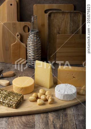 Cheese assorted on a wooden board, rustic style. Several varieties of whole cheese: parmesan, tilsiter, halloumi with spices, camembert, smoked bocconcini, cheddar. Selective focus, close-up. 105879823