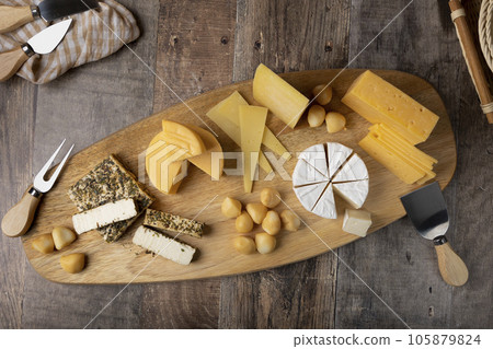 Cheese assorted on a wooden board, rustic style. Several varieties sliced cheeses: parmesan, tilsiter, halloumi with spices, camembert, smoked bocconcini, cheddar. Selective focus, close-up. 105879824