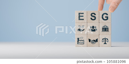 ESG concept of environmental, social and governance. Hand holds wooden cubes with abbreviation ESG standing with other ESG icons on blue background. Copy space. wide banner ESG concept of environmental, social and governance. Hand holds wooden cubes with abbreviation ESG standing with other ESG icons on blue background. Copy space. wide banner 105881096