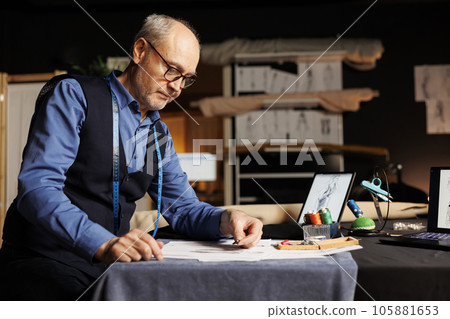 Elderly suitmaker in atelier shop workspace picking perfect sewing materials for upcoming client sartorial comission. Senior couturier choosing fitting buttons for bespoke suit 105881653
