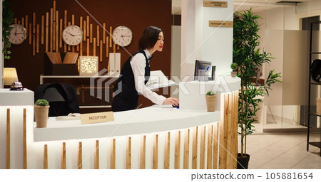 Happy friendly receptionist making phone calls standing at check in counter in welcoming resort lobby. Cheerful professional hotel employee taking booking requests while working at reception desk Happy friendly receptionist making phone calls standing at check in counter in welcoming resort lobby. Cheerful professional hotel employee taking booking requests while working at reception desk 105881654
