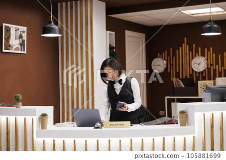 Front desk staff holding pos terminal in hotel lobby, preparing to welcome guests and provide excellent service. Asian receptionist using device for electronic payment at luxury resort. Front desk staff holding pos terminal in hotel lobby, preparing to welcome guests and provide excellent service. Asian receptionist using device for electronic payment at luxury resort. 105881699